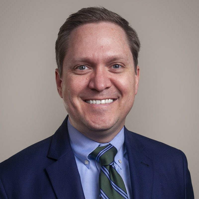 Image of Burkett CPAs Vice President Daniel Crowson, smiling, wearing a blue suit, blue shirt and striped tie