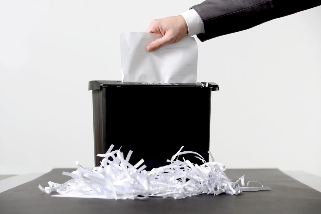 person in a suit putting paper in a shredder
