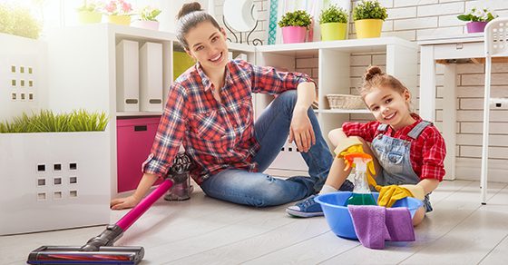 woman and young child smiling in house with cleaning supplies