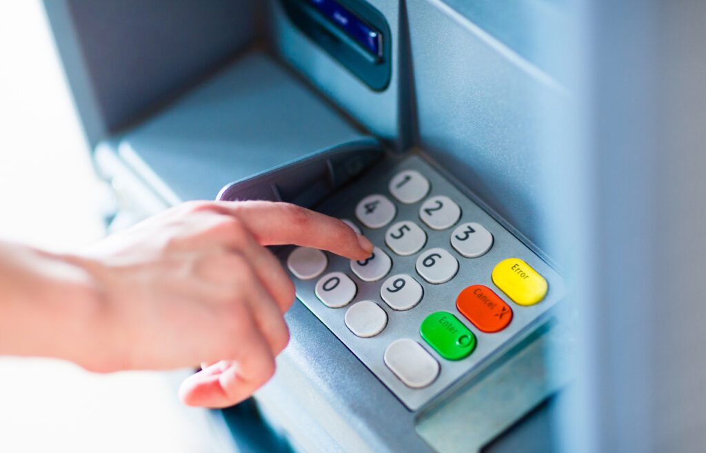 Close-up of hand entering PIN/pass code for a money transfer, on a ATM/bank machine keypad outside. IP PIN